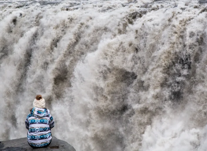 Photo d'une personne assise devant la cascade Dettifoss en Islande